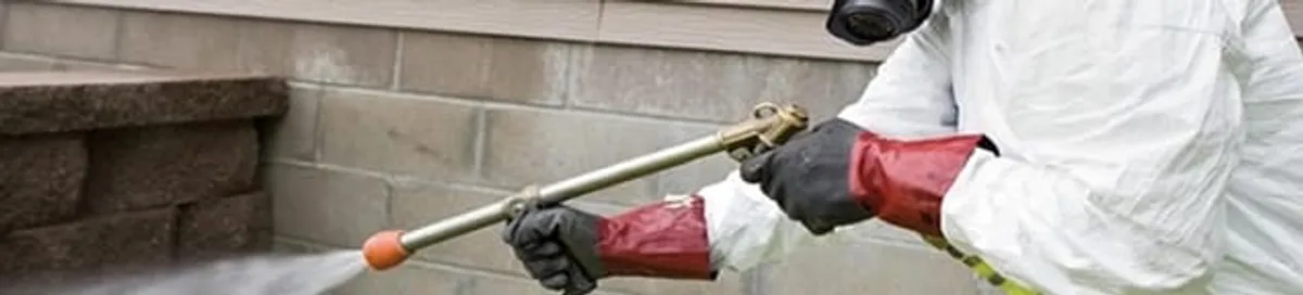 Pest control technician applying exterior insect treatment along a home foundation in Little Rock, AR
