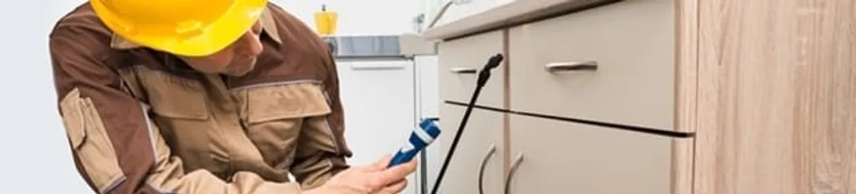 Roach exterminator applying treatment under kitchen cabinets in Little Rock, AR