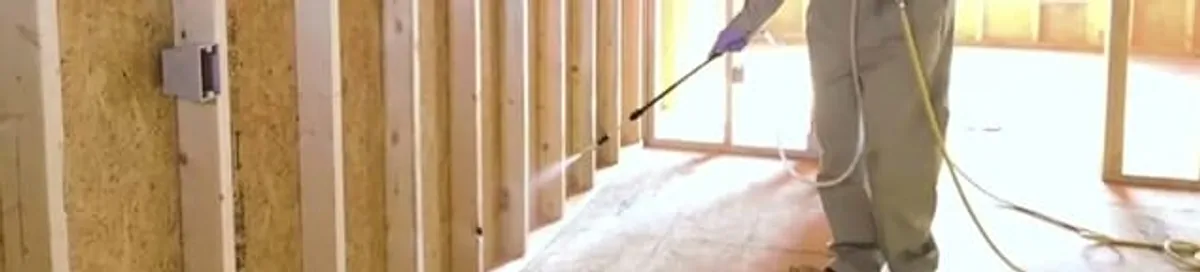 Termite treatment technician applying spray along framing and unfinished walls in Little Rock, AR